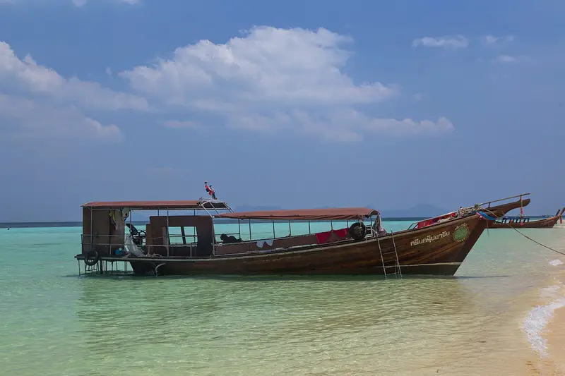 A covered longtail boat anchored in the shallows at Ko Kradan